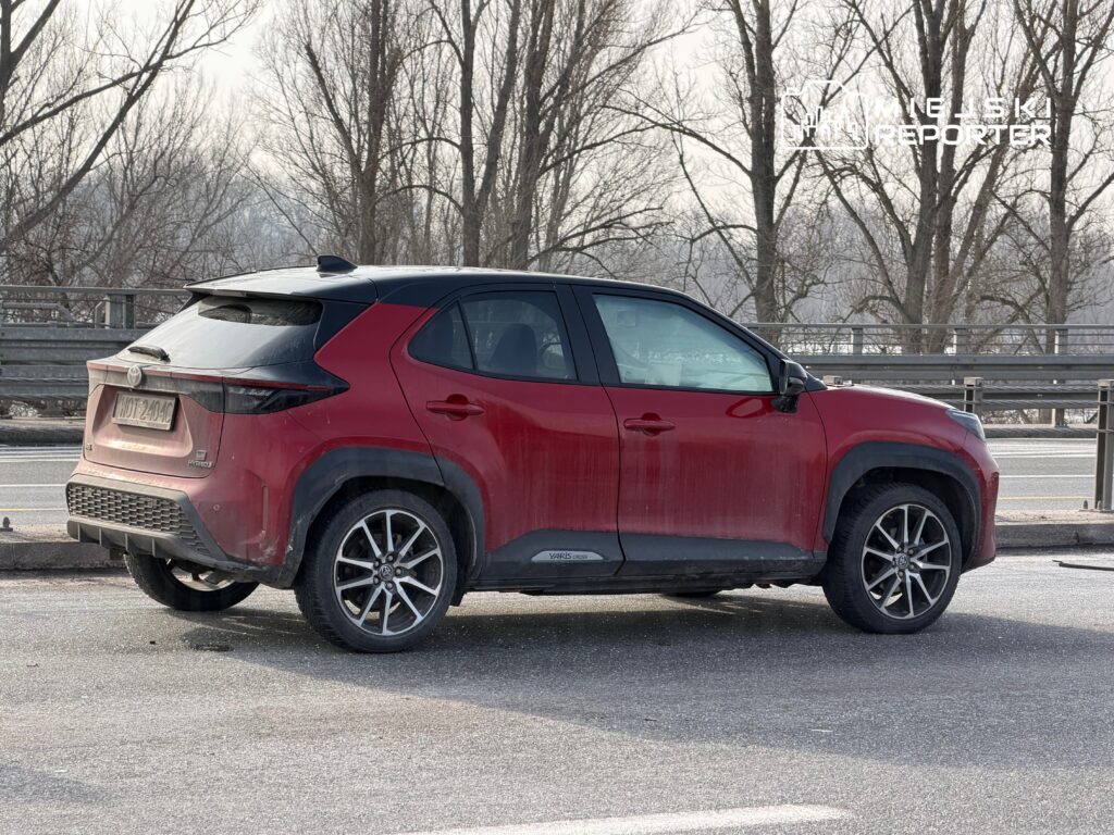 Czerwony SUV zaparkowany na poboczu drogi, z widocznymi zanieczyszczeniami na karoserii i bezpieczną barierką w tle.