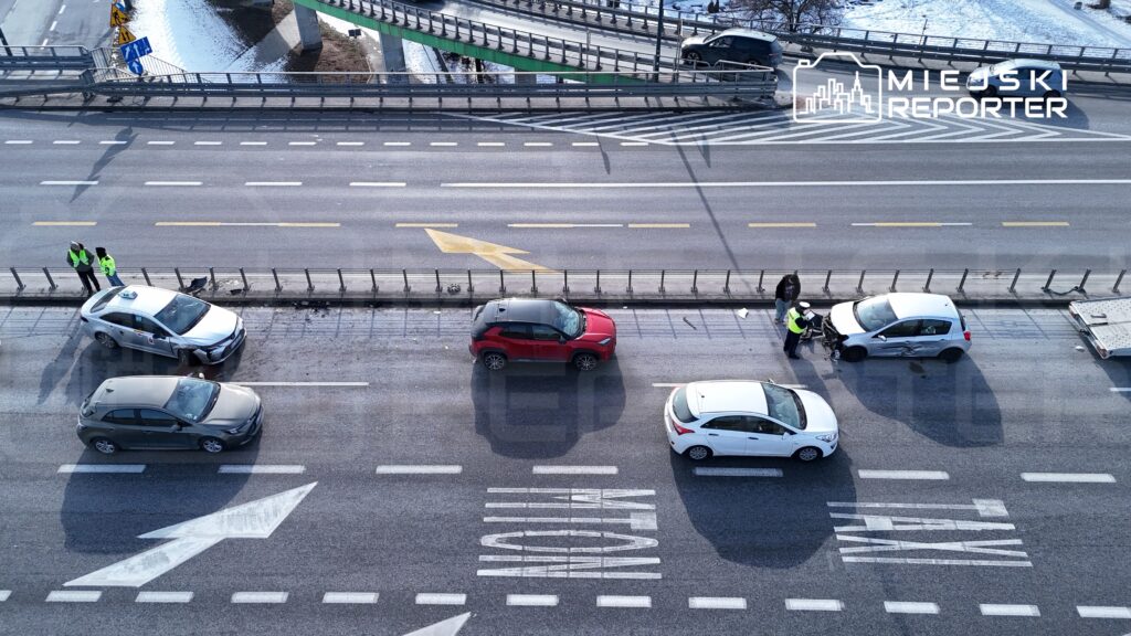 Kierowcy rozmawiają z policjantami obok uszkodzonego samochodu osobowego na ruchliwej ulicy.