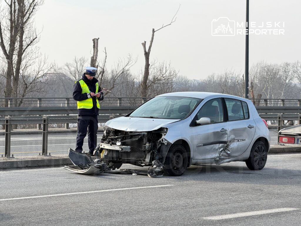 Policjant w kamizelce odblaskowej notuje szczegóły przy zniszczonym samochodzie osobowym na drodze.