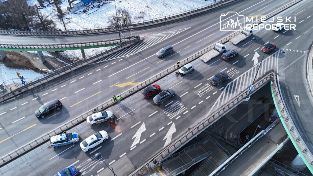 Ruch uliczny na skrzyżowaniu, z pojazdami i policjantami kierującymi ruchem w zimowej scenerii.