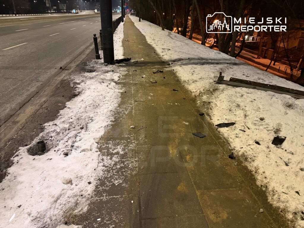 Zniszczony chodnik obok jezdni, pokryty śniegiem i fragmentami materiałów budowlanych.