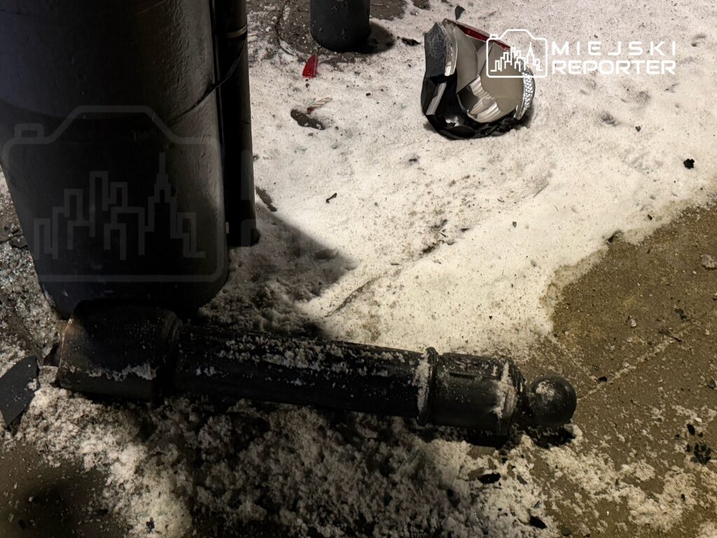 Złamany słupek oświetleniowy leży na zasypanej śniegiem nawierzchni, obok znajduje się uszkodzona lampa.