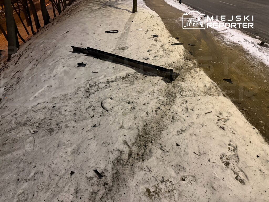 W pobliżu drogi leży uszkodzony element metalowy na zaśnieżonym poboczu, otoczony resztkami materiałów.