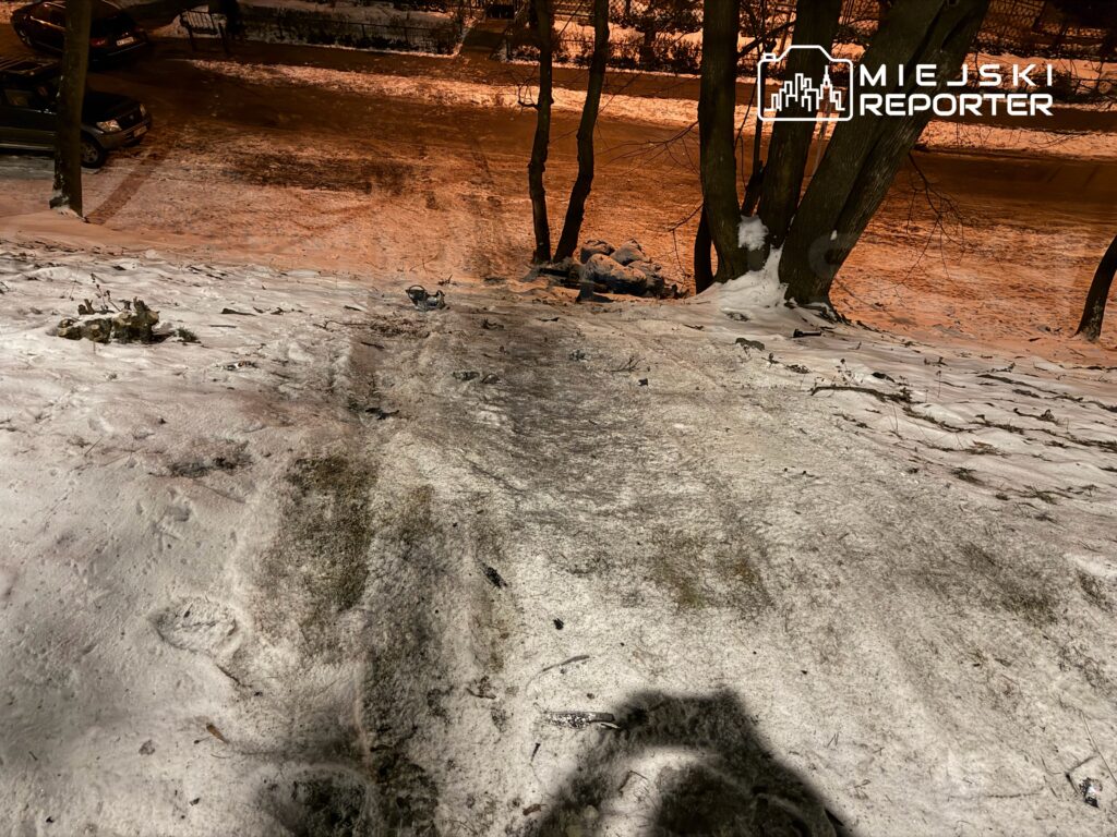 Zbocze pokryte śniegiem z wyraźnymi śladami, w tle widoczne samochody na oświetlonej ulicy.