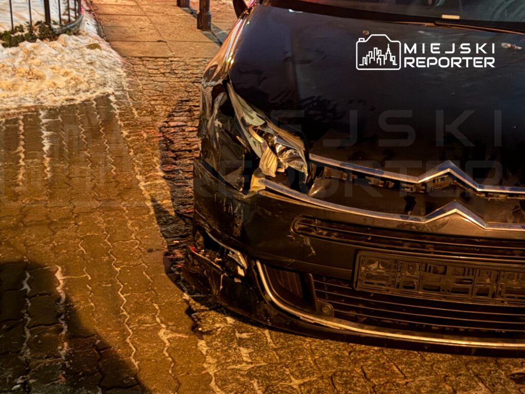 Uszkodzony czarny samochód osobowy zaparkowany na oświetlonej ulicy z kostki brukowej.