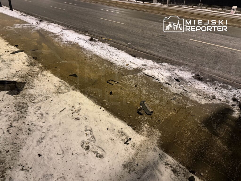 Zniszczona nawierzchnia chodnika z odłamkami i śniegiem, w tle widoczna droga.