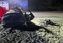 Zniszczony samochód osobowy leży na zaśnieżonej nawierzchni, obok znajduje się sprzęt ratunkowy. W tle widoczny wóz strażacki.