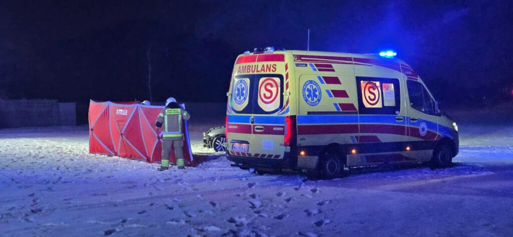 Ratownicy w uniformach przy czerwonym namiocie w zaśnieżonym terenie, obok karetki z włączonymi sygnałami świetlnymi.