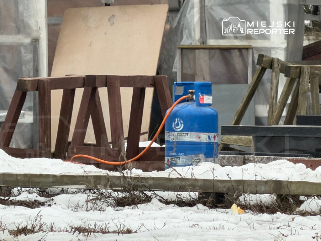Niebieska butla gazowa z wężem leży obok drewnianych stołów w zaśnieżonym otoczeniu.