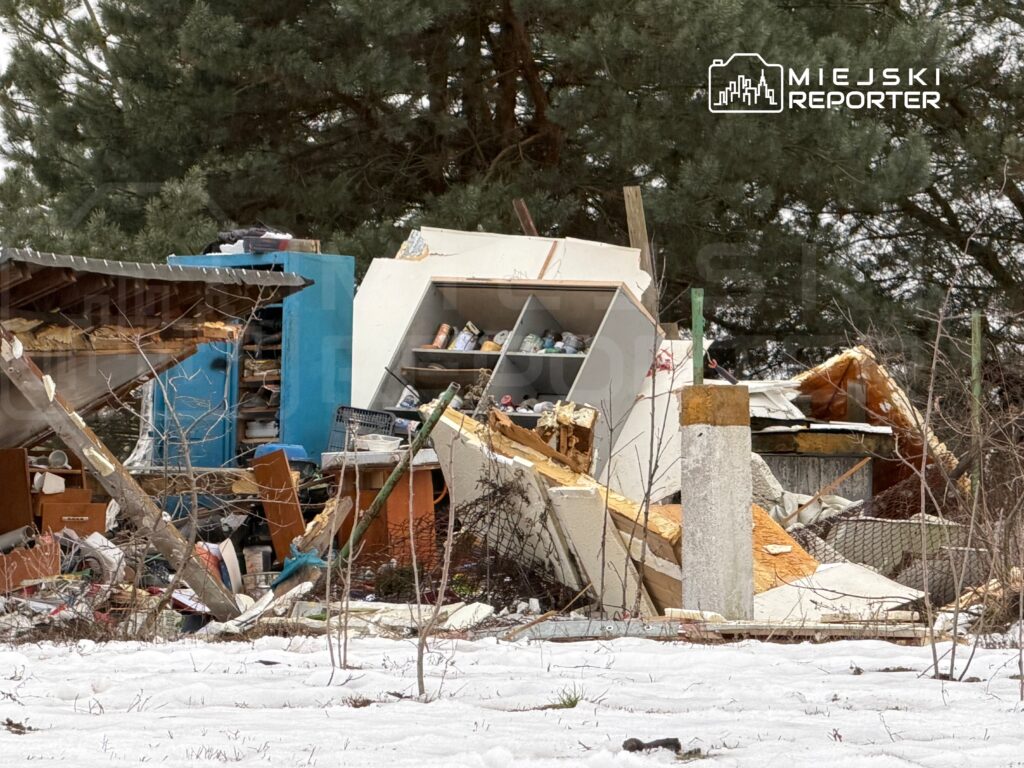 Zniszczony budynek z przewróconym dachem i porozrzucanymi meblami w otoczeniu pokrytym śniegiem.