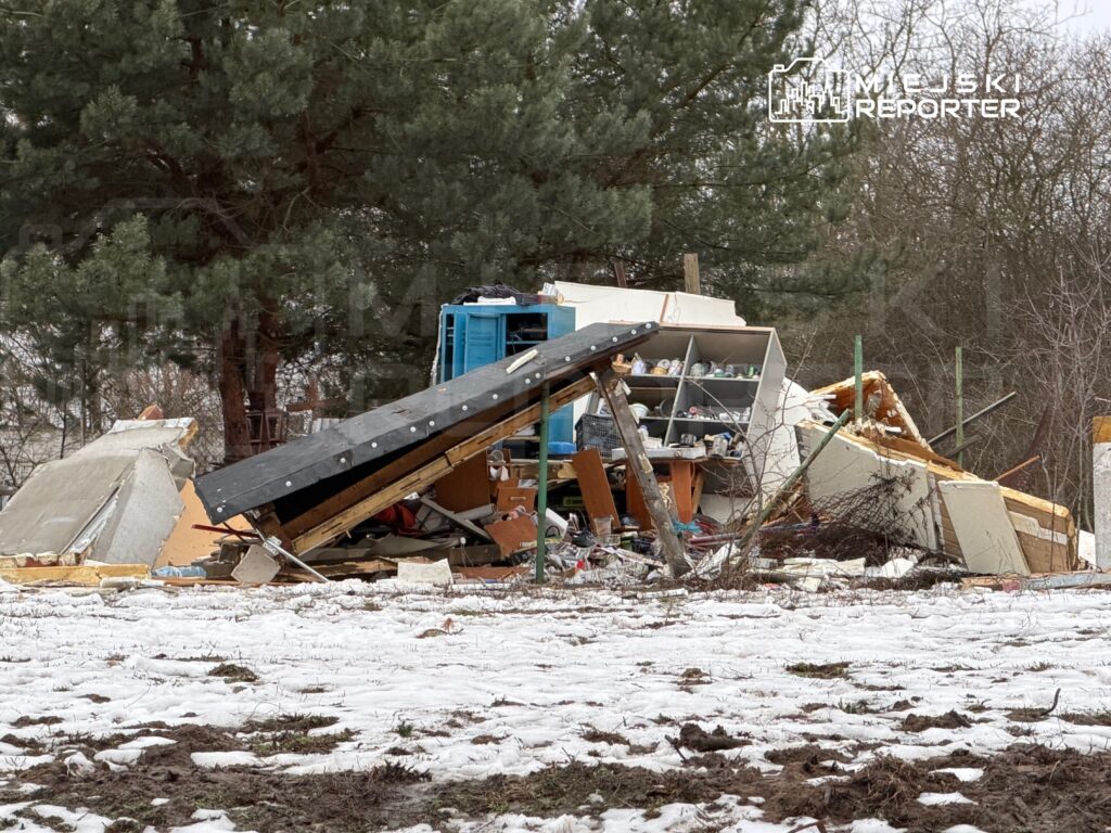 Zniszczony budynek z zawaloną konstrukcją i porozrzucanymi meblami na tle drzew, w otoczeniu leżącego śniegu.