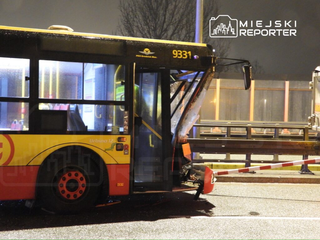 Zniszczony autobus stojący na drodze, z uszkodzoną tylną częścią i widocznymi śladami deszczu.