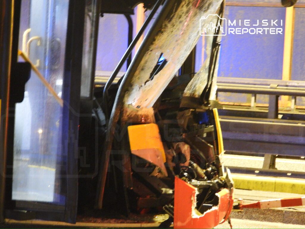 Uszkodzony autobus z wgniecioną przednią częścią stoi na drodze, otoczony przez policyjne światła.