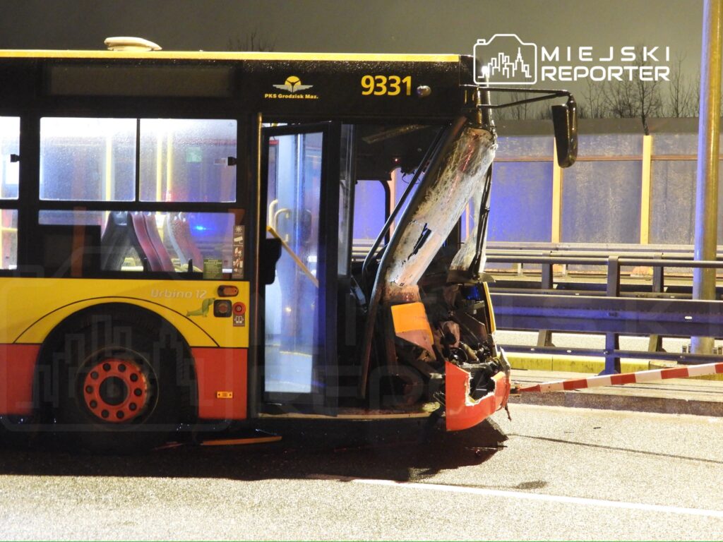 Autobus z uszkodzoną tylną częścią stoi na jezdni, w otoczeniu słabego oświetlenia nocnego.