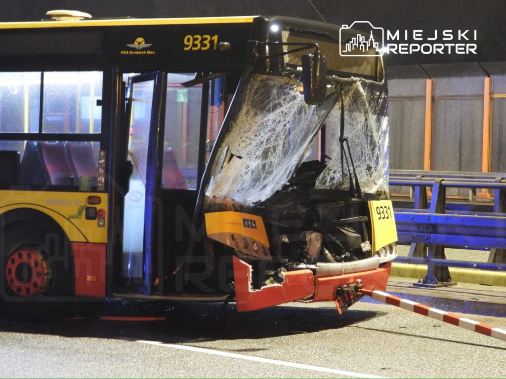 Uszkodzony autobus z widocznym zniszczeniem tylnej części stoi na jezdni, w nocy, pod oświetleniem ulicznym.