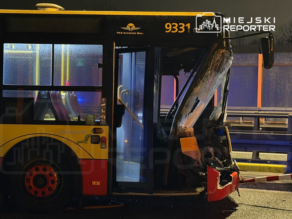 Autobus z uszkodzoną tylną częścią stoi na drodze, w tle widać niebieskie światła policyjne.