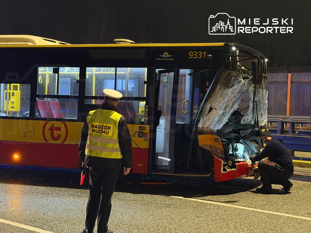 Mężczyzna w kamizelce z napisem "Nadzór Ruchu" obserwuje uszkodzony autobus na drodze w nocy.