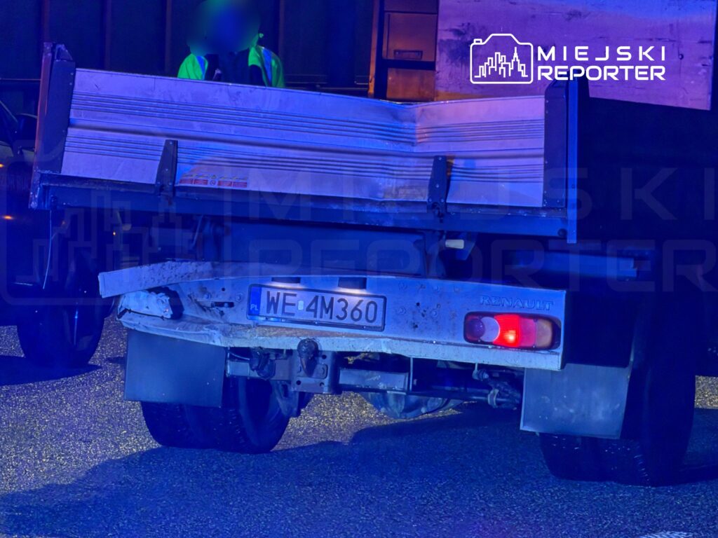 Ciężarówka marki Renault z otwartą skrzynią ładunkową stoi na drodze, w tle widać policyjne światła.