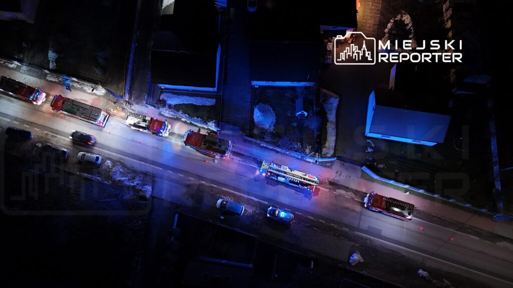 Wielka akcja ratunkowa z udziałem wozów strażackich na oświetlonej ulicy w nocy, z widocznymi niebieskimi sygnalizatorami.