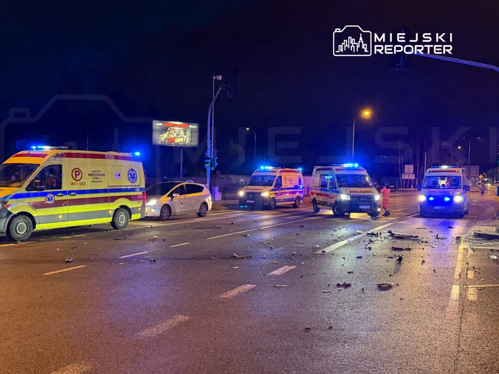 Karetki pogotowia z włączonymi sygnałami świetlnymi stoją na drodze, wokół leżą fragmenty pojazdów.