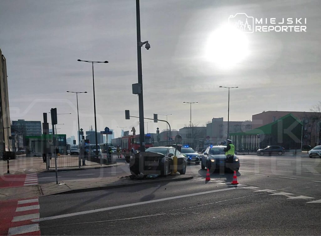 Kierowca w kamizelce odblaskowej kieruje ruchem obok uszkodzonego samochodu na skrzyżowaniu.