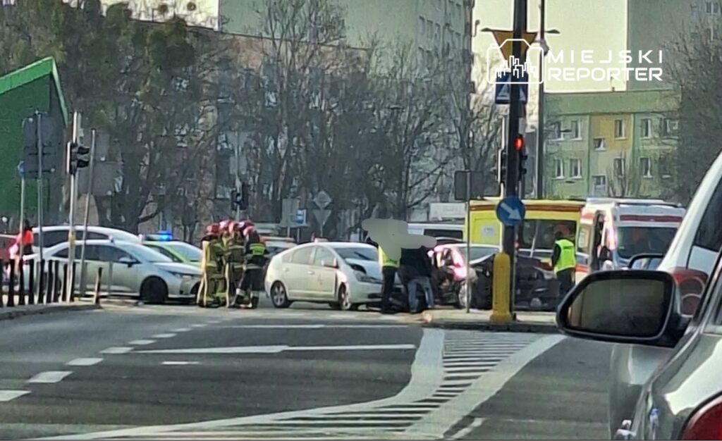 Grupa strażaków udziela pomocy poszkodowanym w wyniku wypadku drogowym na skrzyżowaniu ulic.