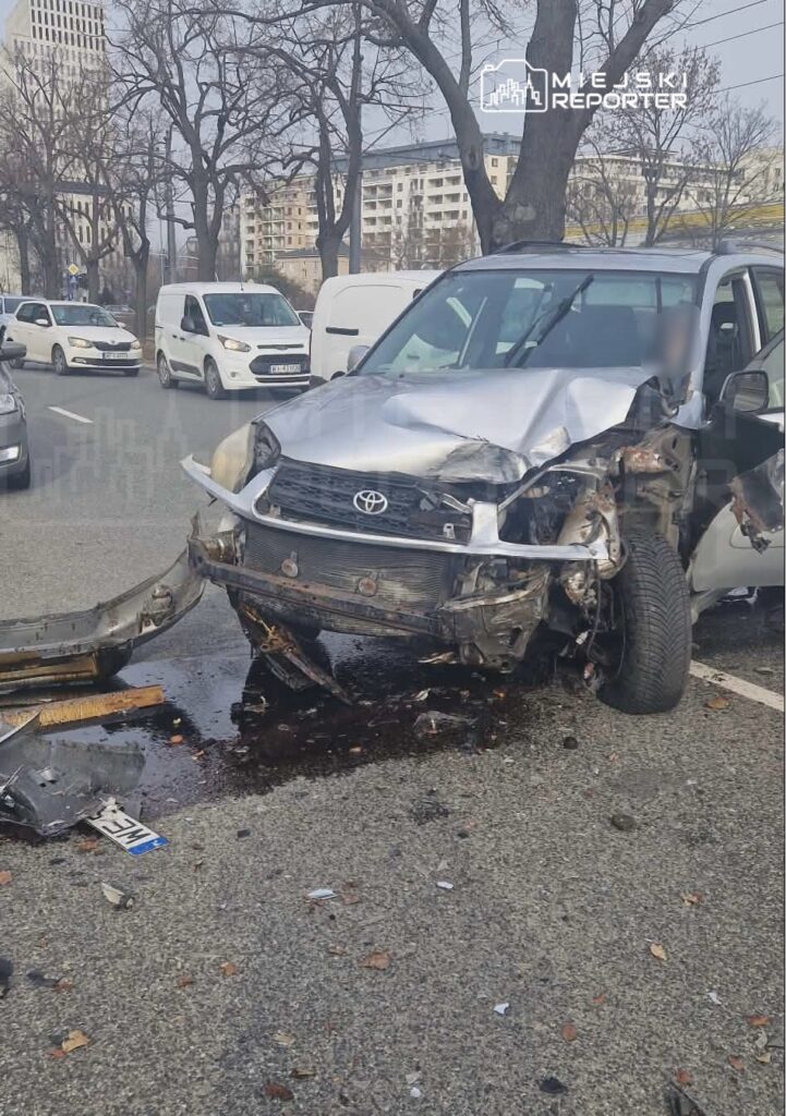 Zniszczony samochód osobowy marki Toyota leży na drodze, obok widoczne inne pojazdy i fragmenty wraku.