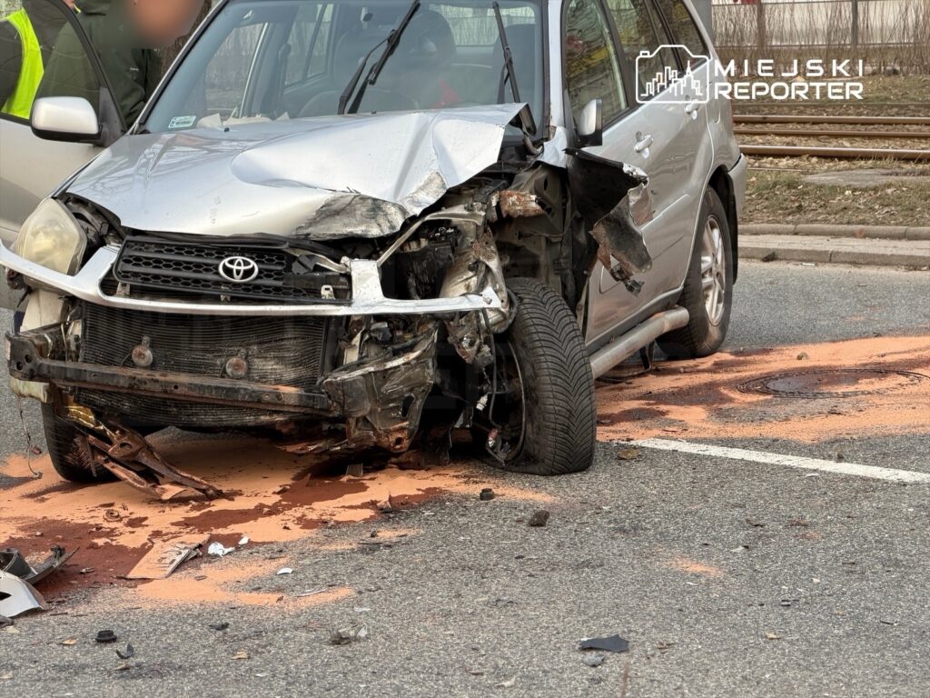 Uszkodzony samochód osobowy marki Toyota z wgniecionym przodem leży na jezdni, obok widoczne plamy płynów.