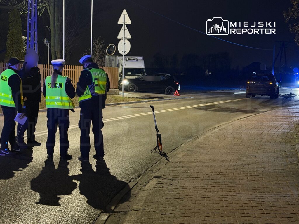 Grupa policjantów w kamizelkach odblaskowych prowadzi rozmowy obok drogi, gdzie stoi skuter i oznakowane pojazdy.