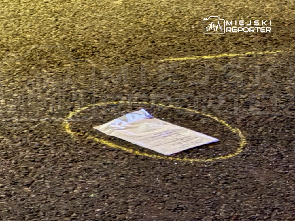 Na jezdni leży biały arkusz papieru otoczony żółtym kółkiem.