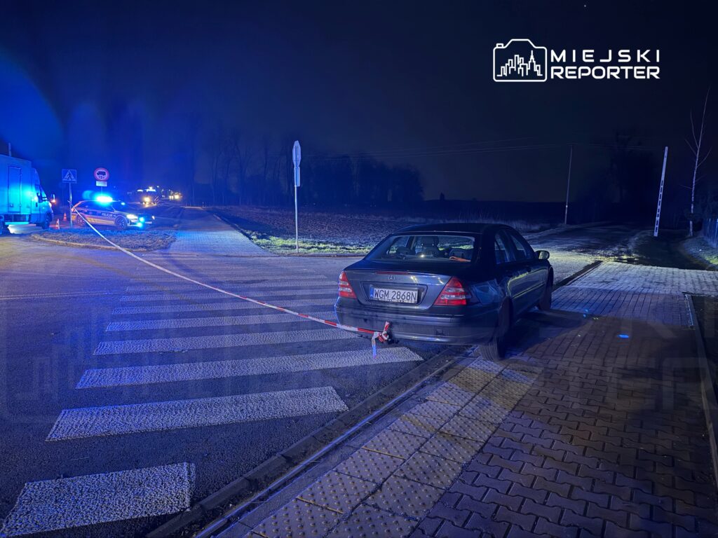 Policyjny radiowóz z włączonymi sygnałami świetlnymi stoi obok zaparkowanego samochodu na drodze, w nocy.