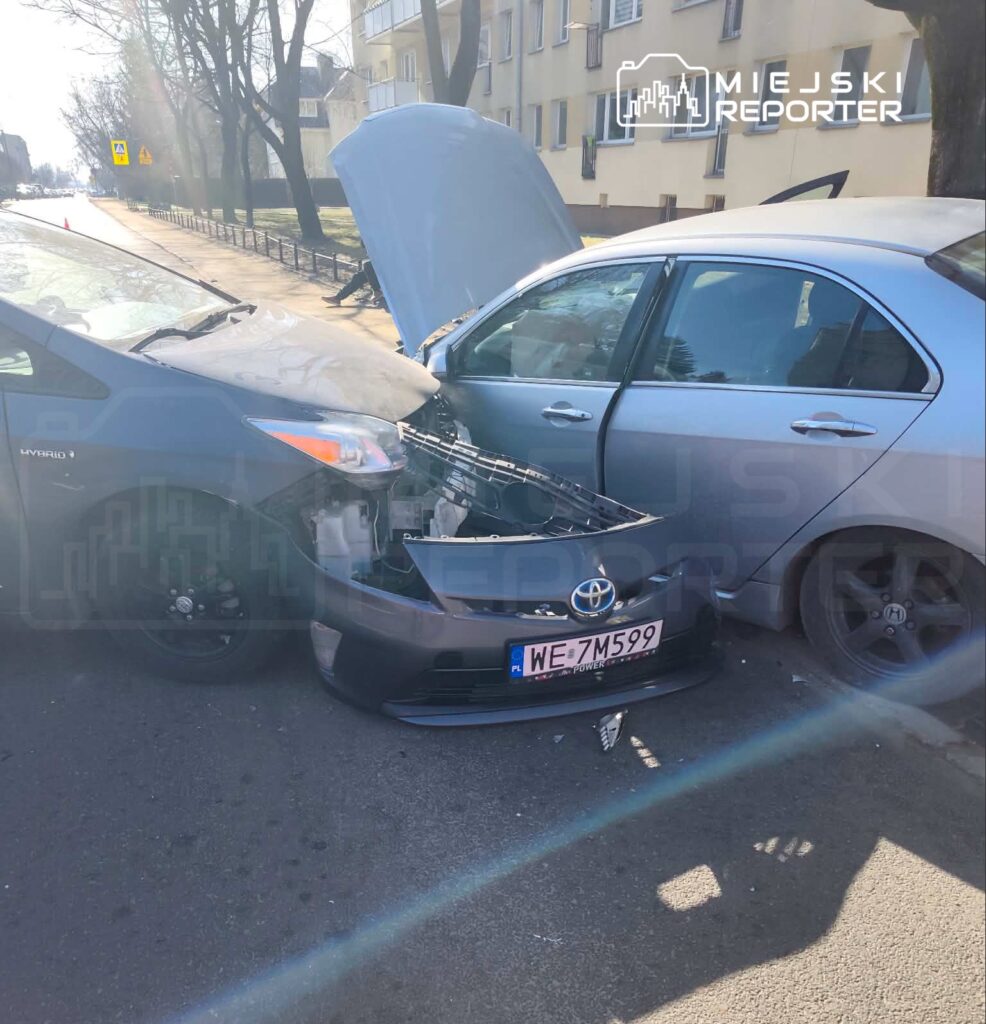 Dwa uszkodzone samochody osobowe zderzone na ulicy; jeden z pojazdów ma otwartą maskę.