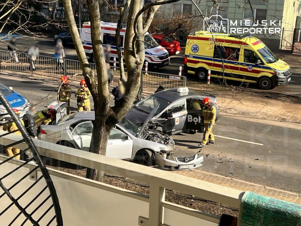 Na ulicy doszło do wypadku samochodowego, w którym zderzyły się dwa pojazdy. Strażacy udzielają pomocy poszkodowanym.