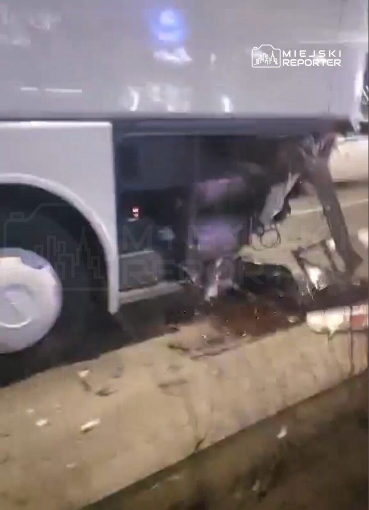 Uszkodzony autobus z otwartą boczną klapą, wylewająca się ciecz na jezdnię, w miejskim otoczeniu.