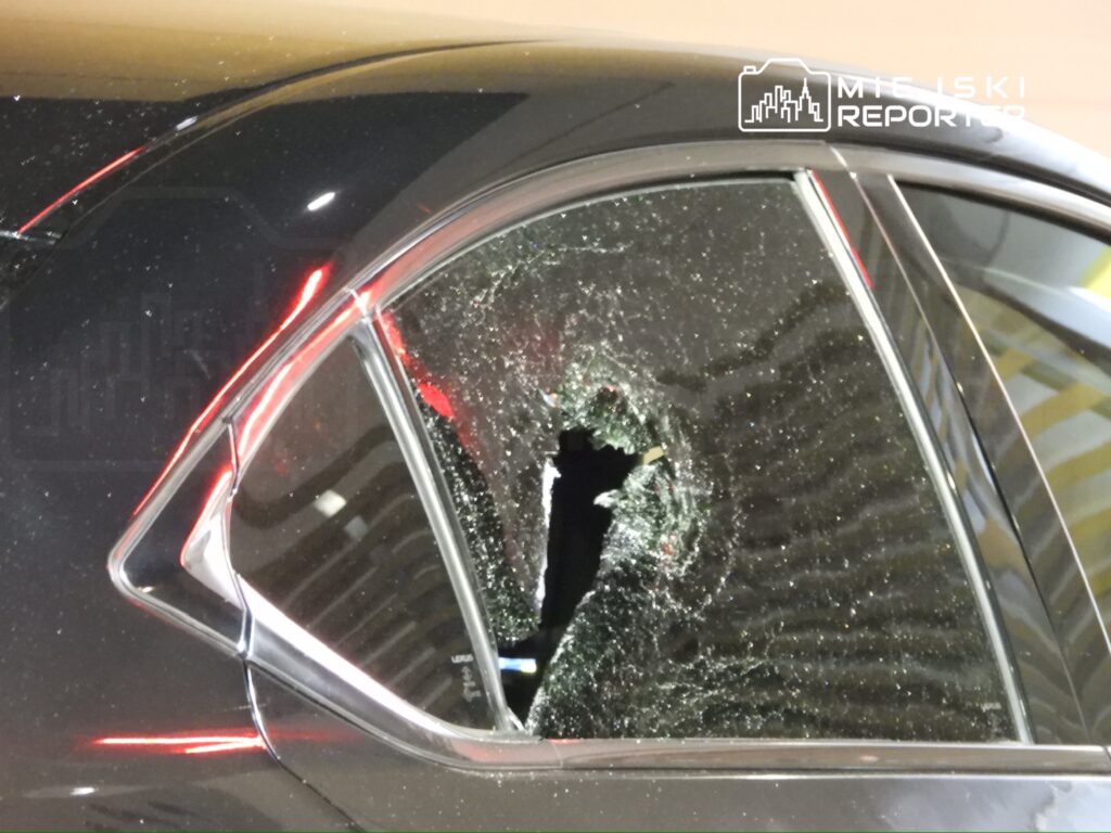 Uszkodzone okno w czarnym samochodzie z dużym otworem, wokół którego znajdują się odłamki szkła.