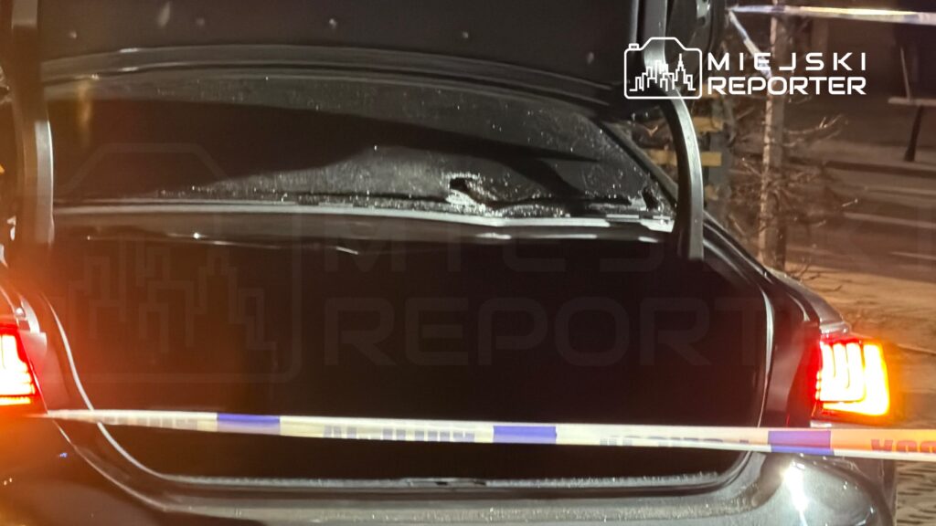 Otwarty bagażnik samochodu z widocznymi śladami uszkodzeń, otoczony policyjnym taśmą zabezpieczającą.