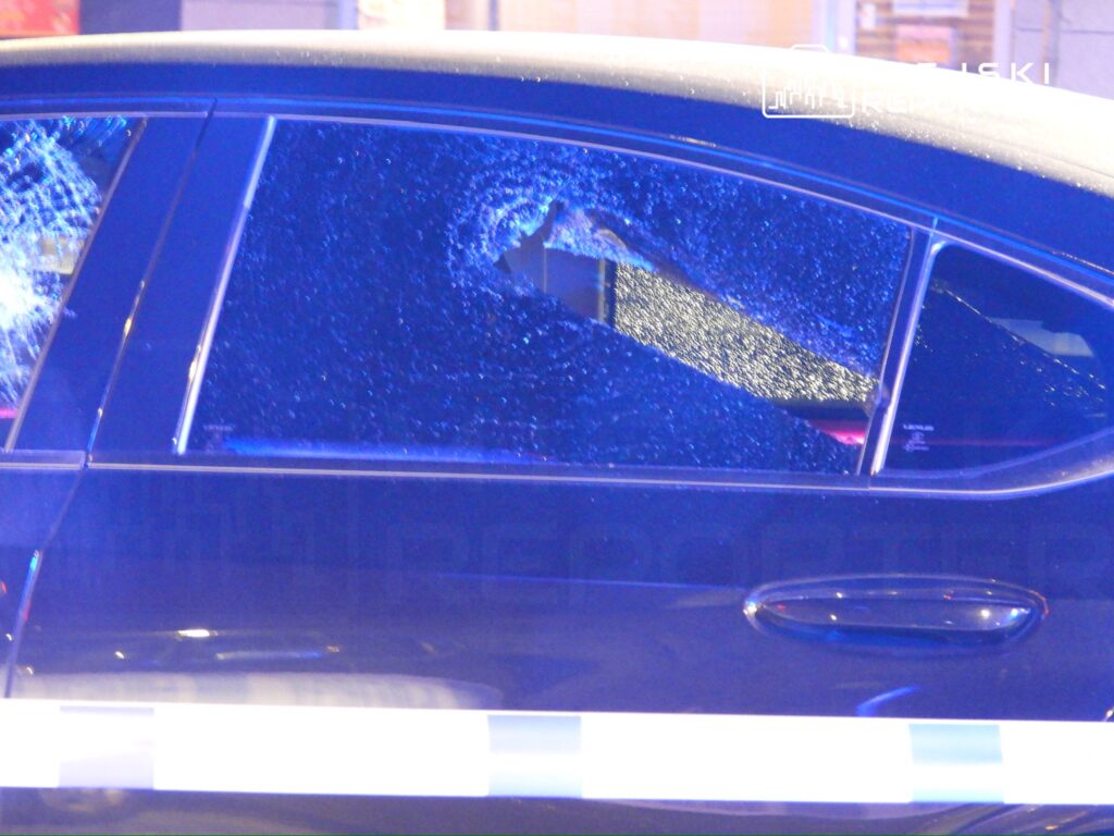 Pęknięta szyba w czarnym samochodzie osobowym oświetlona niebieskimi światłami policyjnymi.