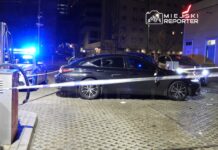 Czarny samochód osobowy stoi na stacji paliw, obok policyjny radiowóz z włączonymi światłami.