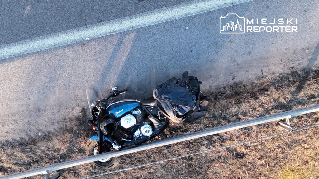 Motocykl marki Indian zaparkowany na poboczu drogi, obok leży czarna torba.