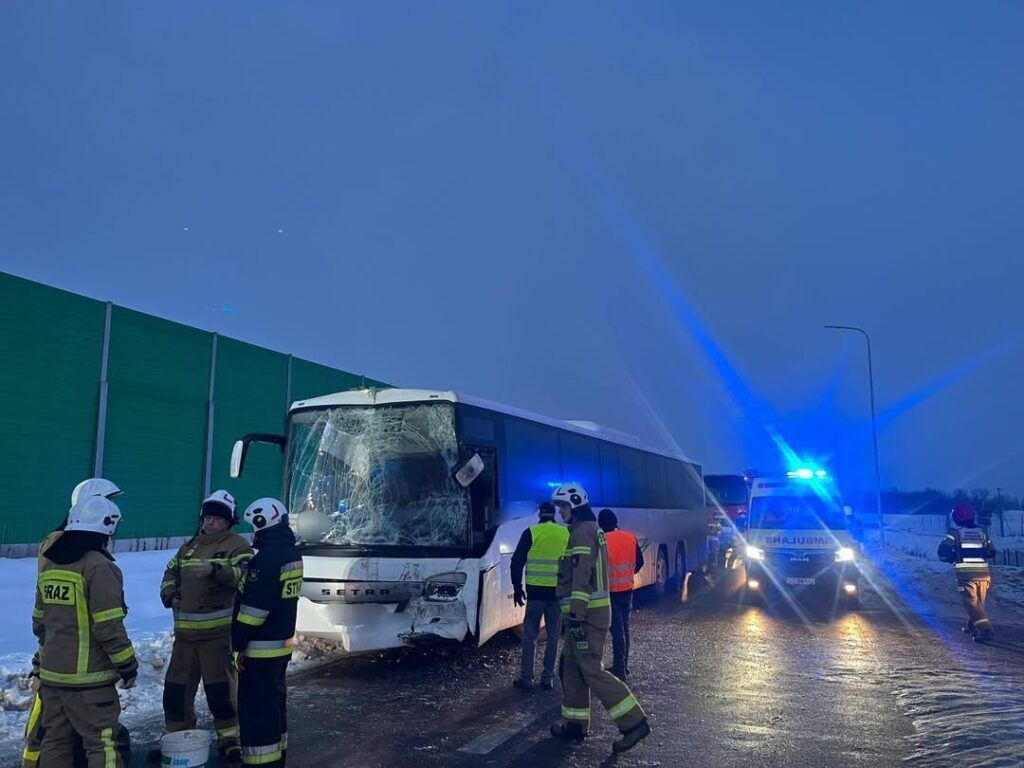 Grupa strażaków w ubraniach ochronnych prowadzi działania ratunkowe przy uszkodzonym autobusie na zaśnieżonej drodze.