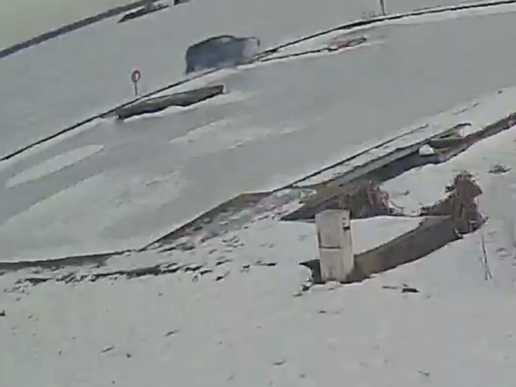 Samochód przejeżdża po zaśnieżonej drodze, w tle widoczne znaki drogowe i fragmenty zamarzniętej nawierzchni.