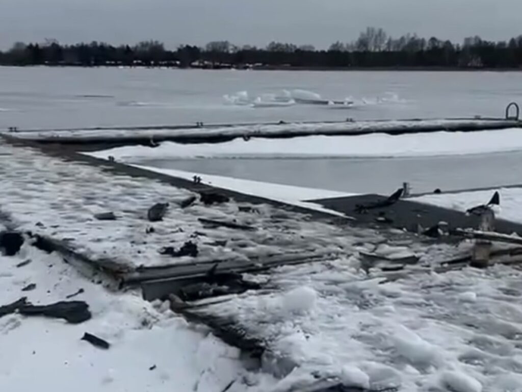 Zniszczona platforma wędkarska pokryta śniegiem i lodem, w tle zamarznięta woda i drzewa.