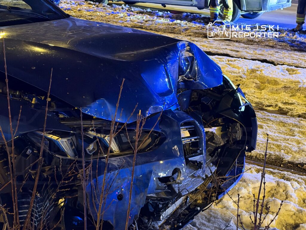 Uszkodzony niebieski samochód osobowy z wgniecionym przodem, stojący w śniegu obok drogi.