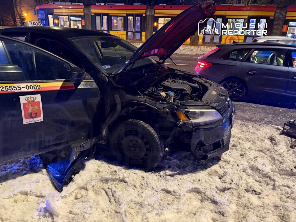 Uszkodzone taksówka z otwartą maską stoi na zaśnieżonej ulicy, obok przejeżdża inny samochód.