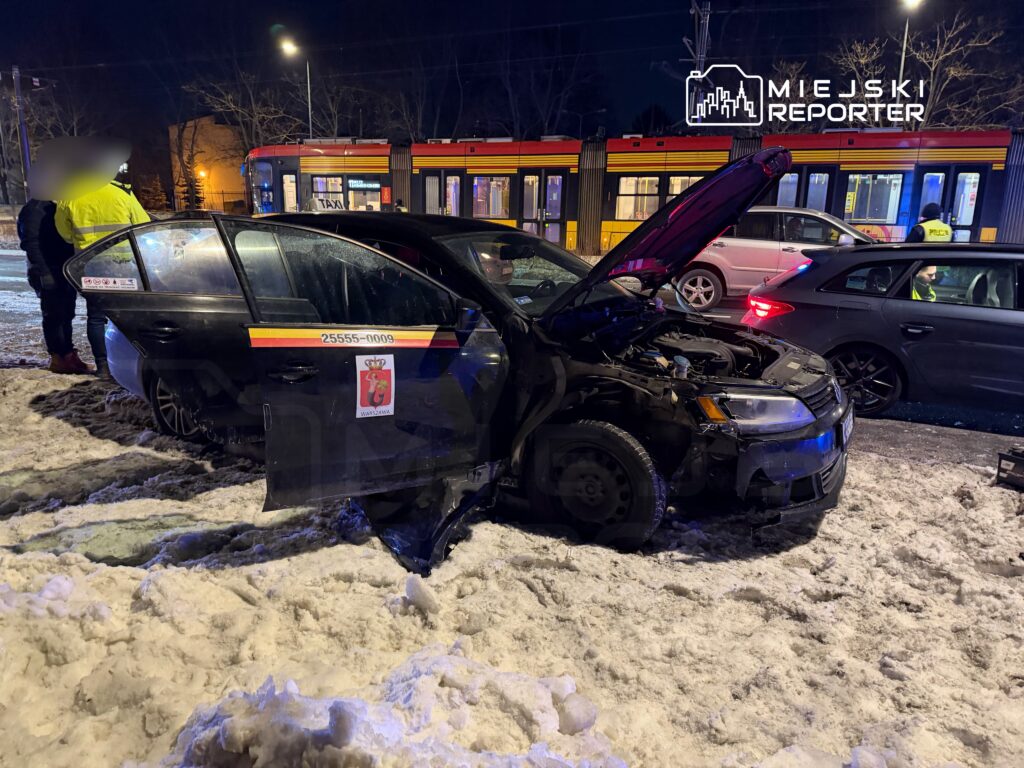 Czarny samochód osobowy z otwartą maską stoi na zaśnieżonej ulicy obok przystanku tramwajowego, obok dwóch mężczyzn.