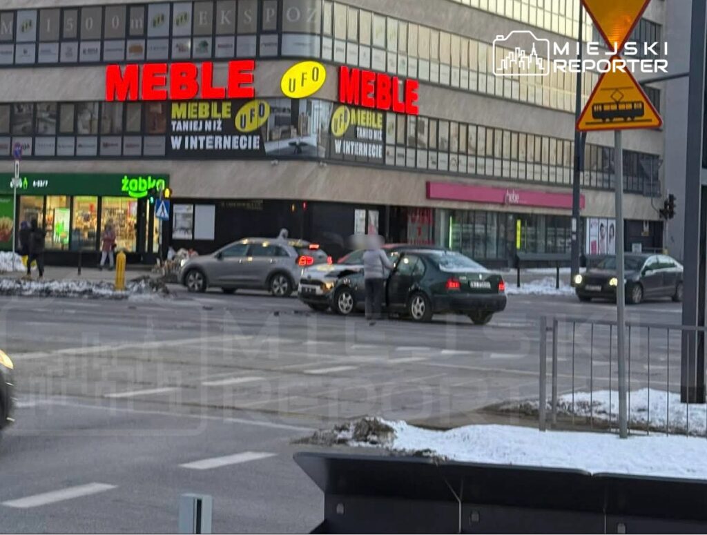 Ruchliwe skrzyżowanie z samochodami zatrzymującymi się na czerwonym świetle obok budynku z reklamą mebli.