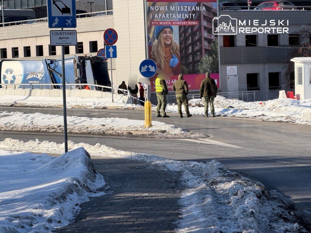 Czterech mężczyzn w mundurach stoi obok wywróconego pojazdu dostawczego na zaśnieżonej drodze.