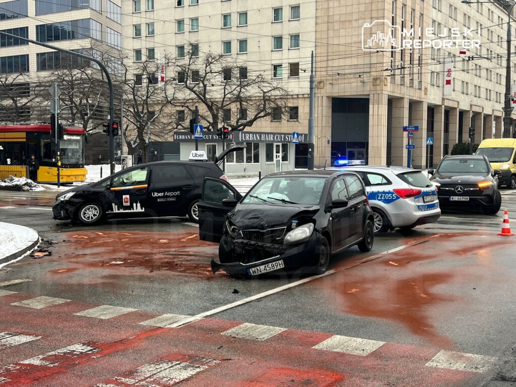 Zderzenie trzech samochodów na skrzyżowaniu, z widocznymi uszkodzeniami i plamami oleju na jezdni.