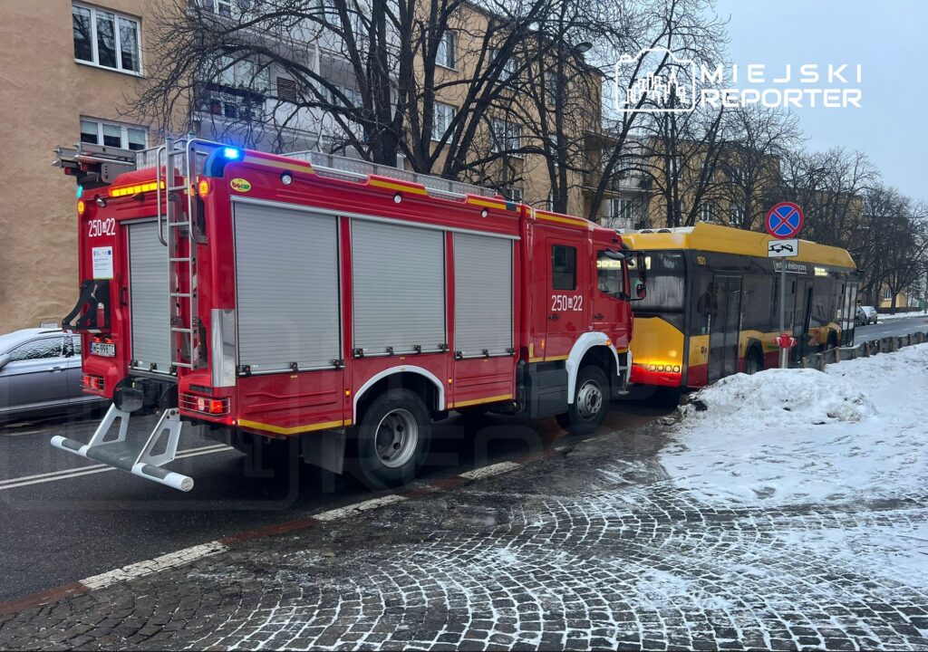 Czerwony wóz strażacki z włączonymi sygnalizatorami stoi obok żółtego autobusu na zaśnieżonej ulicy.