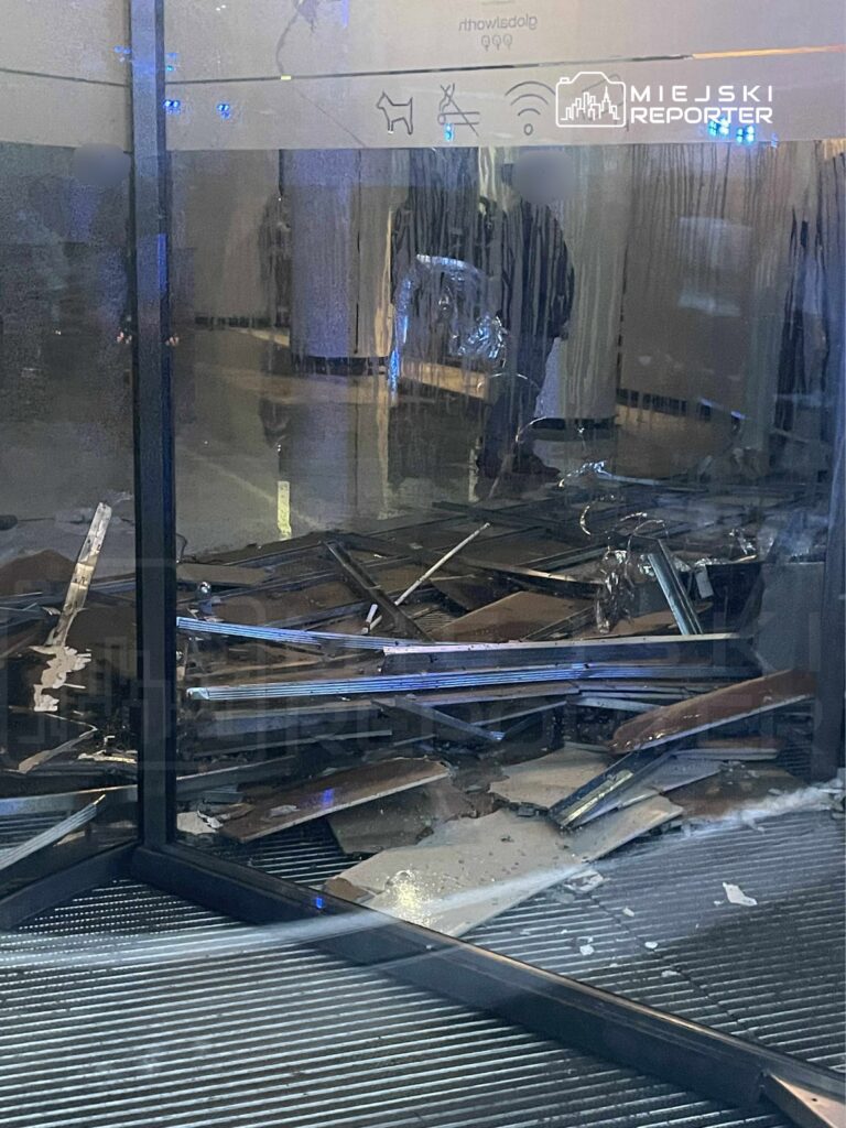 Zniszczona przestrzeń wewnętrzna z porozrzucanymi metalowymi i drewnianymi elementami na podłodze.